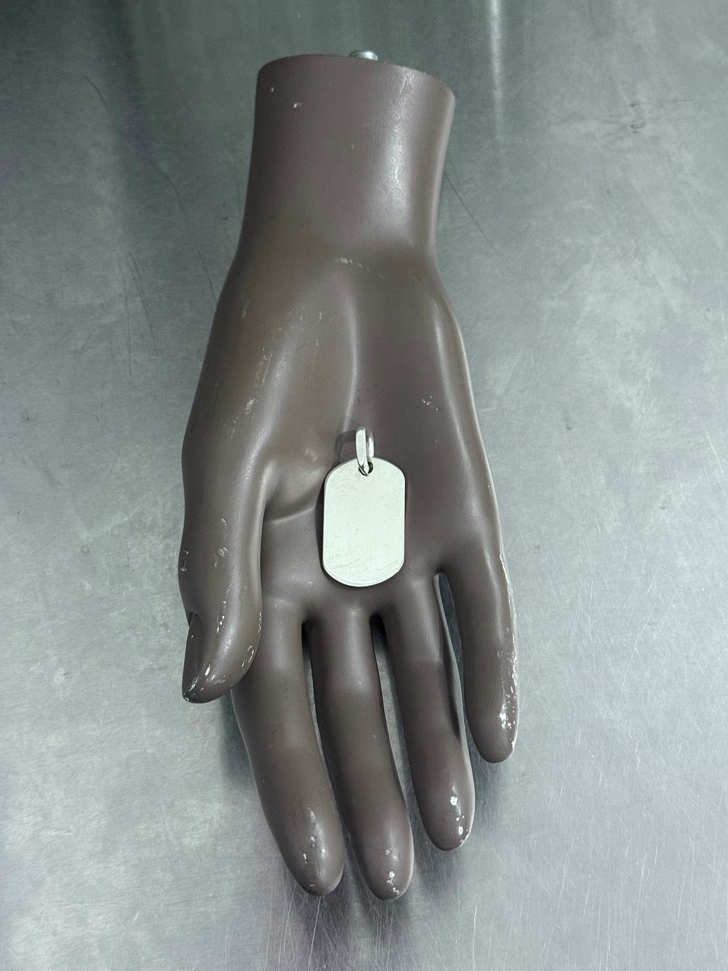 Mannequin hand holding a silver dog tag against a gray background