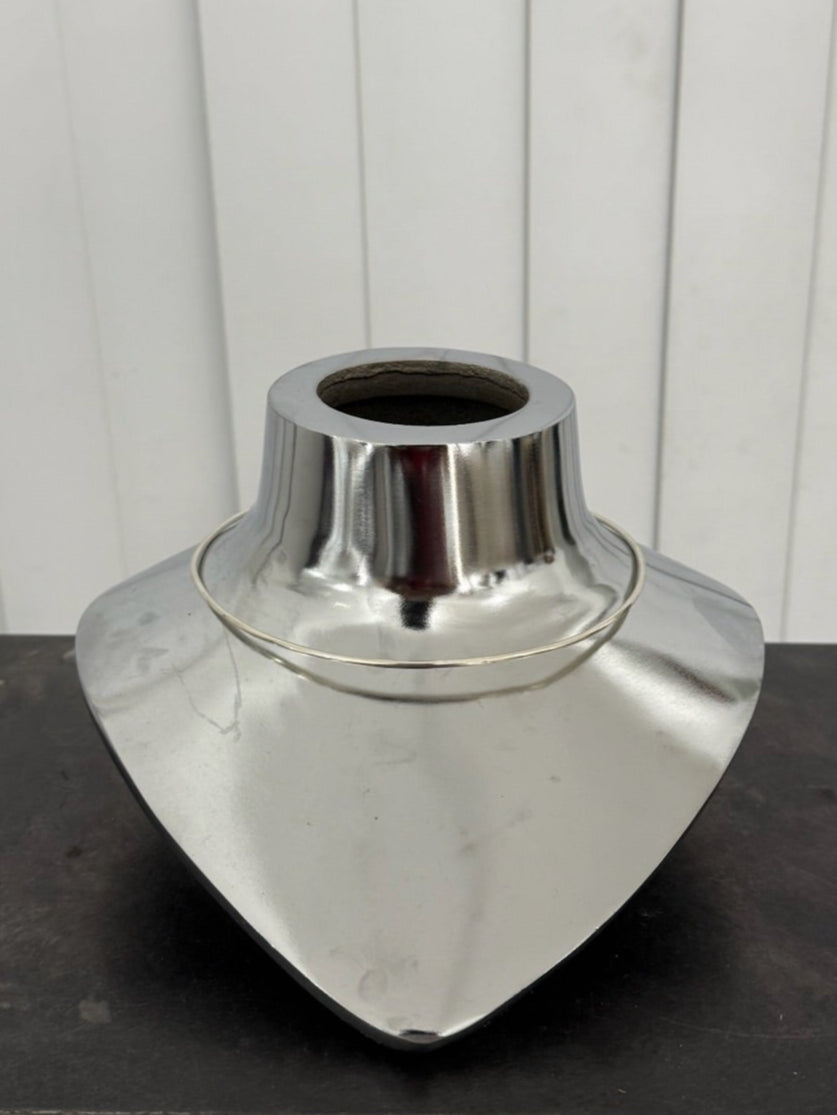 Metallic vase on a black stand against a white paneled wall