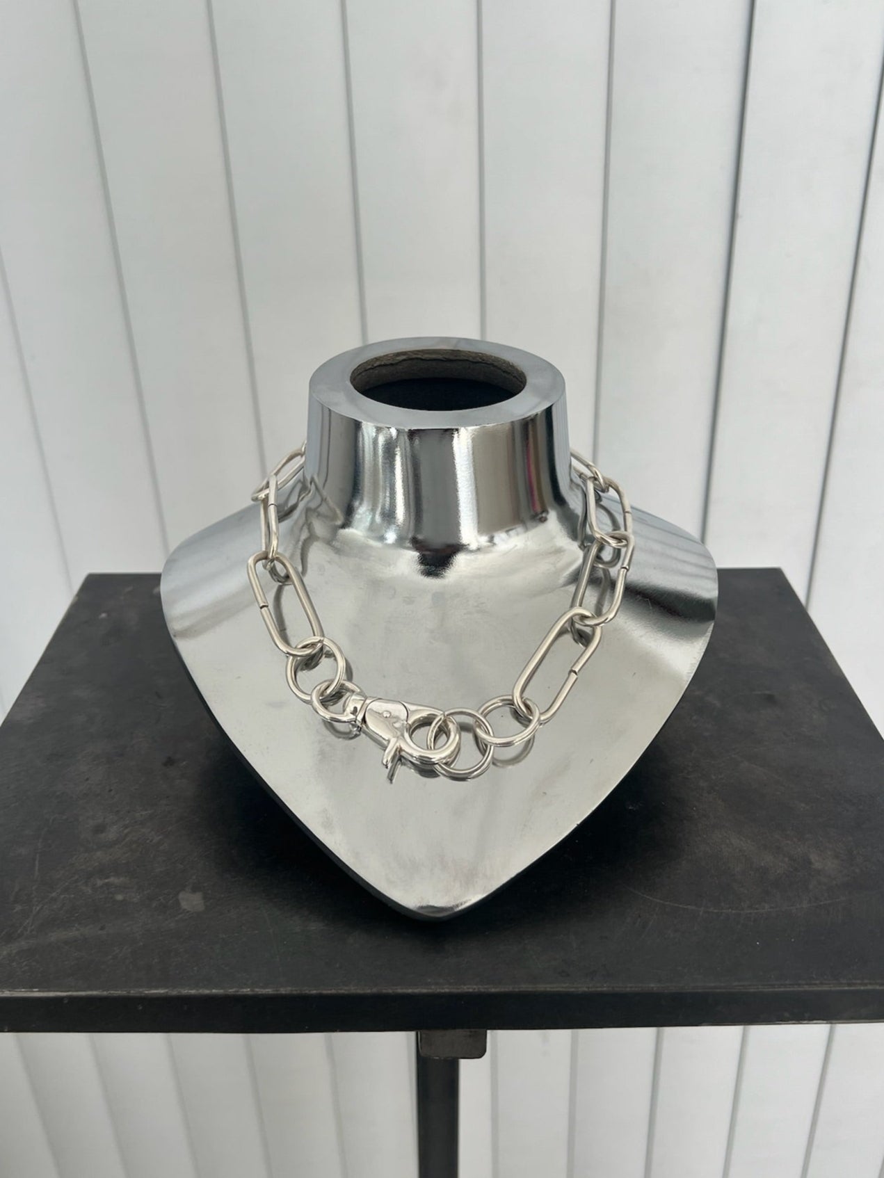 Metallic heart-shaped vase with chain detail on a black surface against a white background