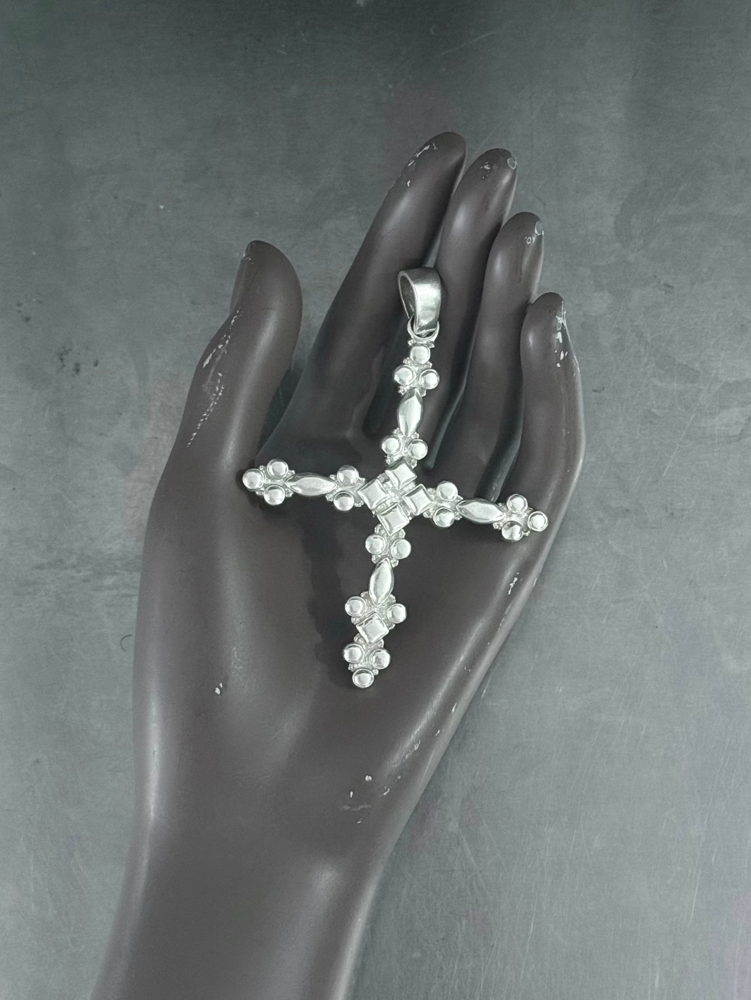 Silver cross-shaped pendant on a black mannequin hand against a dark background