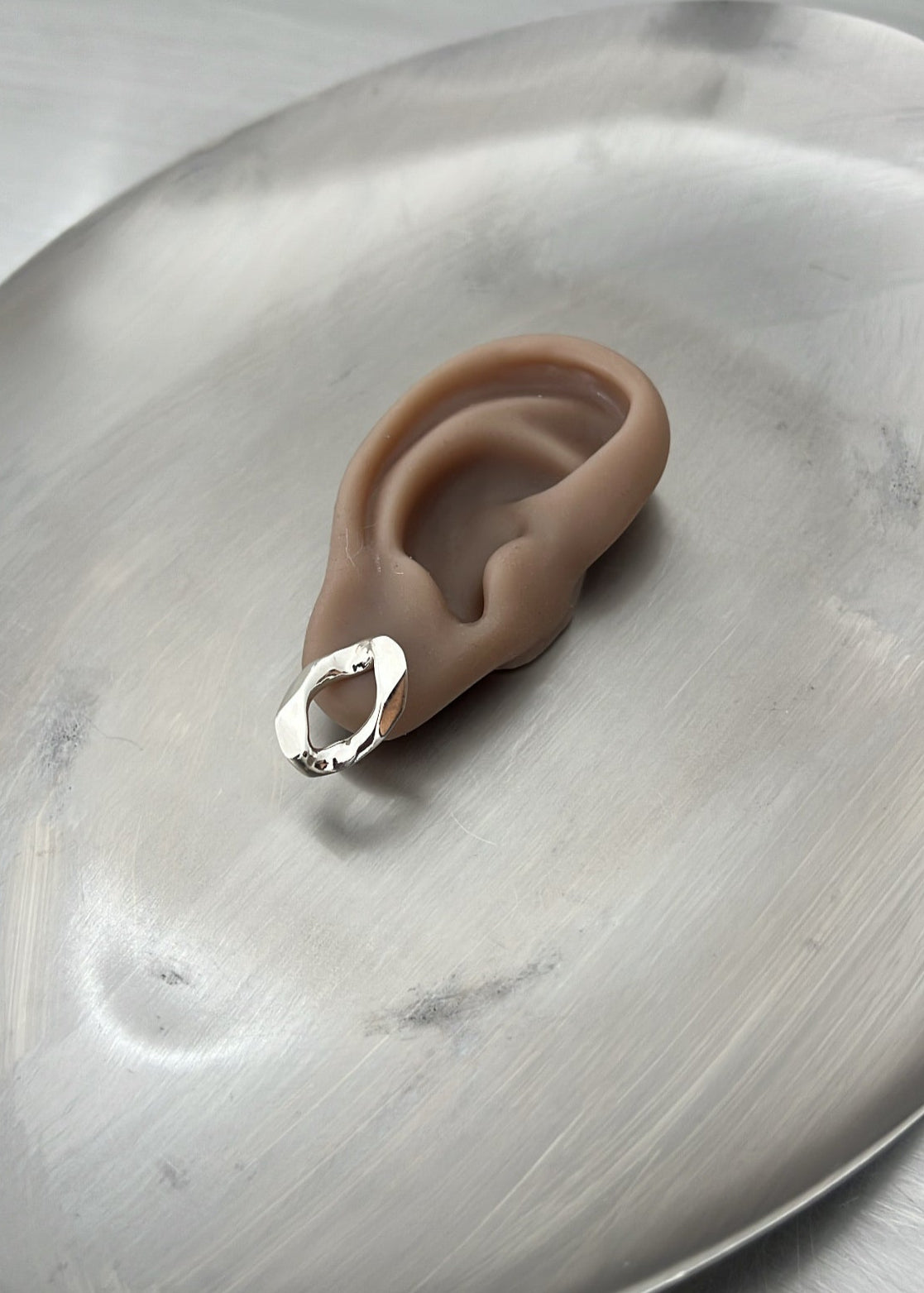 Silicone ear-shaped object with a silver ring on a metallic surface