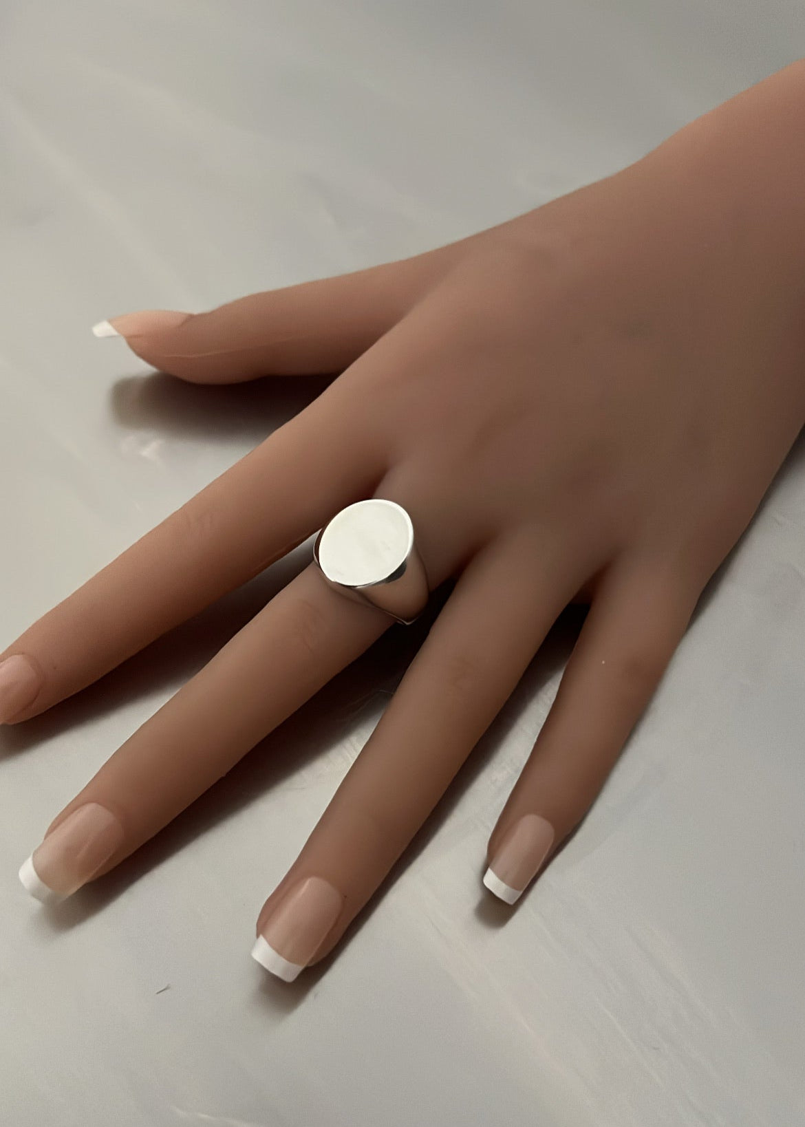 Hand wearing a silver ring on a neutral background