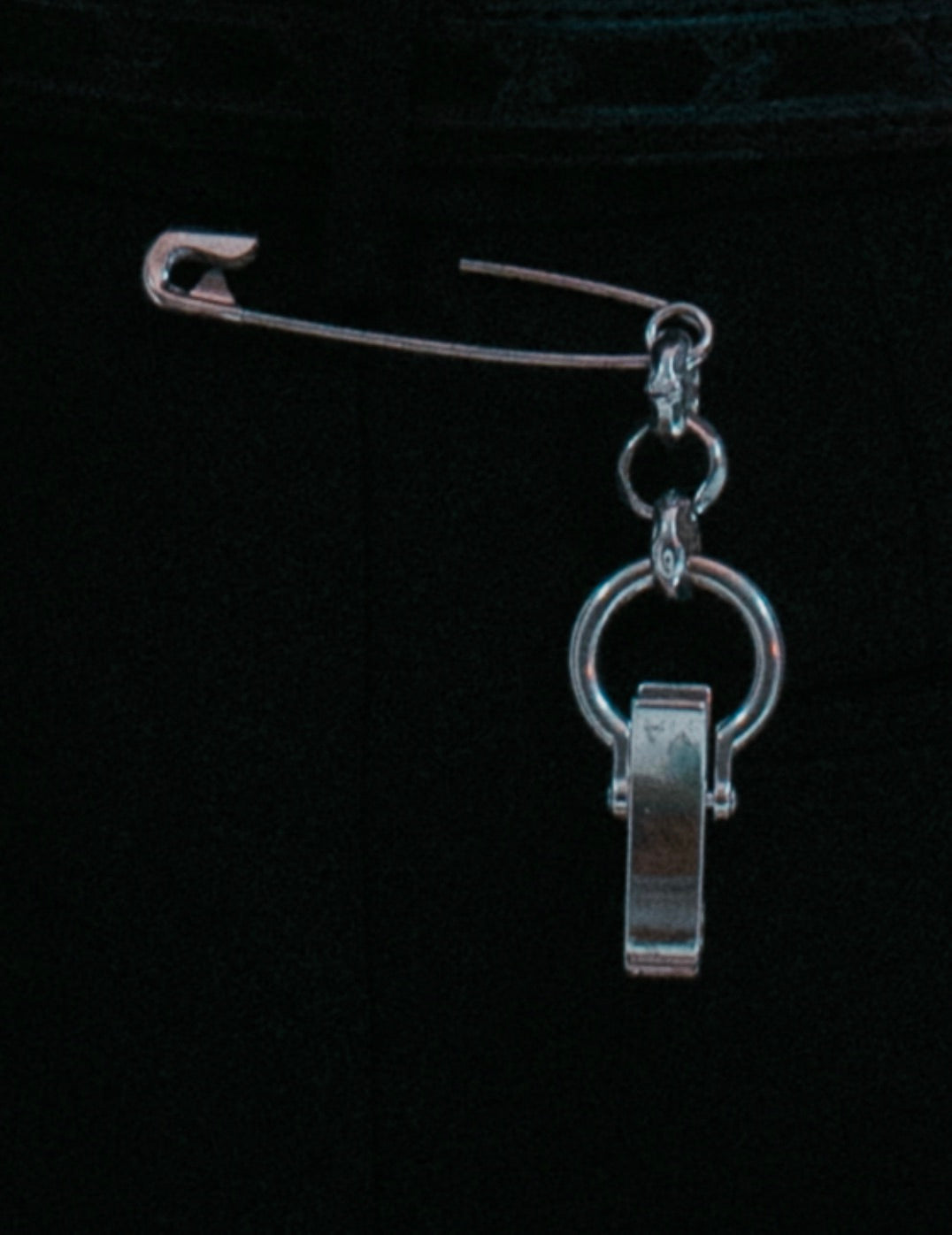 Silver safety-pin style accessory with rolo chain detail . on pants