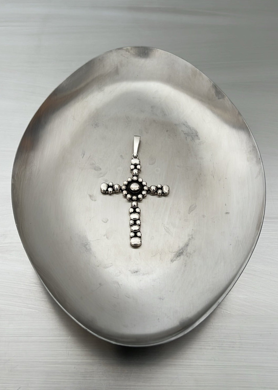 Silver cross pendant on a textured metallic surface
